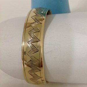 May include: A gold-colored bangle bracelet with a geometric pattern of triangles.