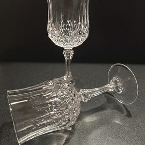 May include: Two clear glass goblets featuring a faceted diamond-cut pattern on the lower bowl and a vertical fluted design on the upper rim. One goblet stands upright while the other rests on its side, both showing a multi-faceted stem.