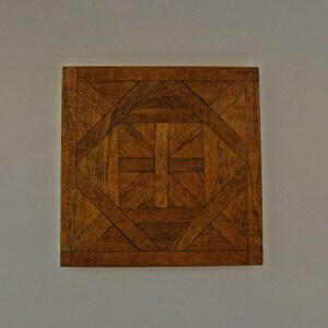 May include: Square wooden tile with a geometric pattern. The tile features a repeating design of interlocking shapes in various shades of brown, creating a visually appealing texture. The tile is likely for flooring or decorative purposes.