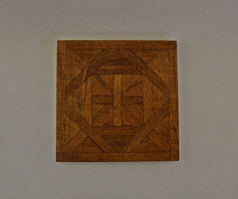 May include: Square wooden tile with a geometric pattern. The tile features a repeating design of interlocking shapes in various shades of brown, creating a visually appealing texture. The tile is likely for flooring or decorative purposes.