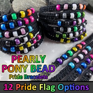 May include: A stack of 12 colourful bracelets made with black string and iridescent pony beads. The bracelets are arranged in a rainbow pattern and feature the text "PEARLY PONY BEAD Pride Bracelets" and "12 Pride Flag Options".