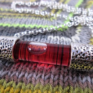 May include: A silver chain necklace with a red glass level pendant. The level is filled with a clear liquid and a small bubble.