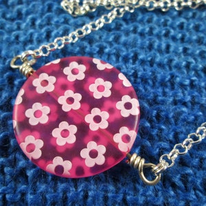 May include: A silver chain necklace with a pink and white floral pendant. The pendant is round and has a glossy finish.