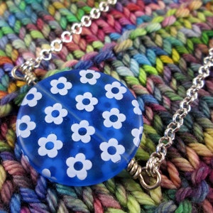 May include: A blue glass bead necklace with a white floral pattern. The necklace is made of silver chain and has a silver clasp.