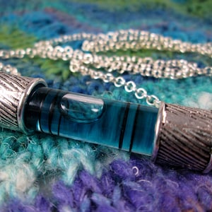 May include: A silver chain necklace with a blue glass level pendant. The level is filled with a blue liquid and has black lines on the side.