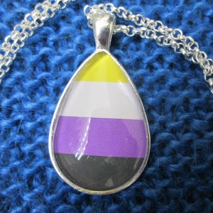 May include: A silver chain necklace with a teardrop-shaped pendant. The pendant is made of glass and features the colors of the non-binary pride flag: yellow, white, purple, and black.