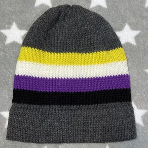 May include: A gray knitted beanie with stripes of yellow, white, purple, and black. The beanie is a symbol of non-binary identity.