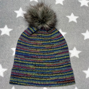 May include: A striped knit beanie with a faux fur pom pom. The beanie is blue, green, red, and black.