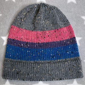 Peut inclure: Un bonnet en tricot gris avec des rayures roses, violettes et bleues. Le bonnet a une texture mouchetée.