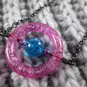 May include: A pink glitter ring with a blue glitter ball inside, hanging from a black chain.