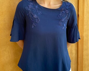 May include: A navy blue blouse with a ruffled sleeve and floral embroidery. The blouse has a round neckline and a slightly A-line shape.