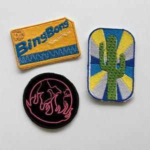 May include: Three embroidered patches: a rectangular yellow patch with blue text reading BingBong, a circular black patch featuring a pink outline of a flame, and a vertical rectangular patch depicting a green cactus against a sunburst background.
