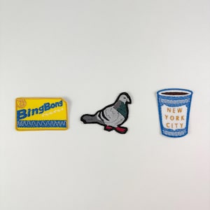 May include: Three embroidered patches: a yellow rectangle with "BingBong" text, a gray pigeon with red feet, and a blue coffee cup with "New York City" text. All patches have a stitched border.