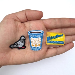May include: Three embroidered patches: a gray pigeon with red feet, a blue cup with text, and a yellow rectangle with "BingBong" in blue. The patches are on a light background.