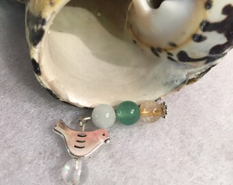 May include: A silver bird charm with a pink body and black stripes hangs from a beaded necklace. The necklace features green, light blue, and orange beads.