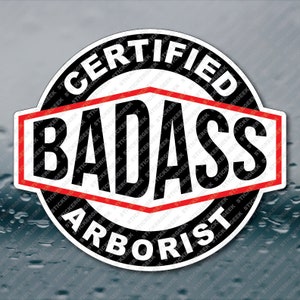May include: A black and white sticker with red accents. The sticker reads "Certified Badass Arborist".