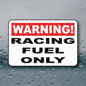May include: Rectangular sticker with a white background and black rounded corners. The top section is red with the word "WARNING!" in white. Below, the text "RACING FUEL ONLY" is in black, bold font.
