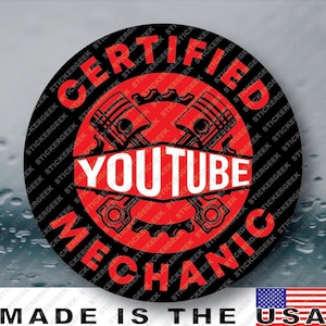 May include: A circular sticker with a black background and a red central emblem featuring a stylized engine piston design. The text "CERTIFIED" appears in red at the top, "YOUTUBE" in white across the center, and "MECHANIC" in red at the bottom.