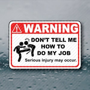 May include: A red and white warning sign with a black exclamation point and a black silhouette of two people fighting. The sign reads "WARNING DON'T TELL ME HOW TO DO MY JOB Serious injury may occur."