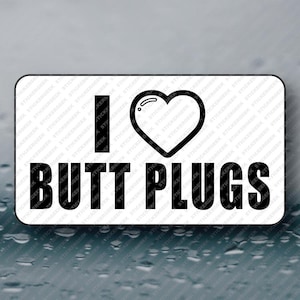 May include: A rectangular sticker with rounded corners. The sticker features the words "I" and "BUTT PLUGS" in black, with a black heart symbol between them. The background is white.