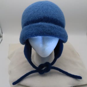 May include: A blue winter hat with ear flaps and a knotted tie closure. The hat is made of a soft, textured material and is displayed on a mannequin head. The ear flaps extend down and are tied under the chin.