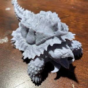 Könnte beinhalten: Ein 3D-gedrucktes Modell einer Schnappschädel-Schildkröte mit einer detaillierten, strukturierten Schale und einem weit geöffneten Maul. Das Modell ist in hellgrau lackiert.