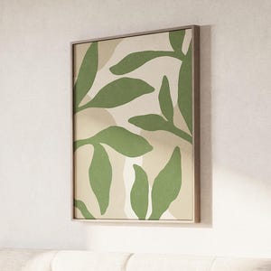 May include: Abstract art print featuring green leaf shapes on a beige background with a light brown frame. The artwork has a minimalist design with organic shapes and a neutral color palette, suitable for home decor.