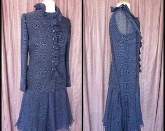 May include: A navy blue dress with white polka dots and a ruffled collar and back. The dress has a flared skirt and long sleeves.