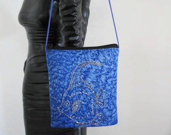 May include: A blue crossbody bag with a silver fish design. The bag has a black strap and a zipper closure.
