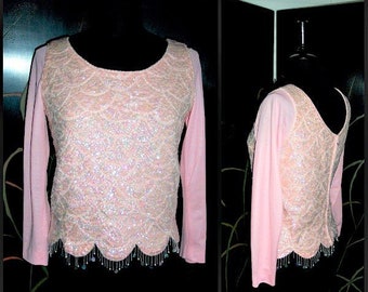 May include: A pink long-sleeved top with a sequined bodice and a scalloped hemline. The top has a beaded trim around the hem.