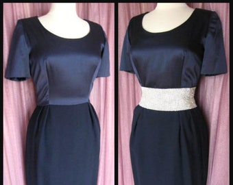 May include: A navy blue dress with a satin bodice and a skirt made of a different fabric. The dress has a rhinestone belt.