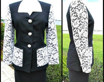 May include: A black skirt suit with white lace sleeves and pockets. The jacket has a white collar and three pearl buttons.