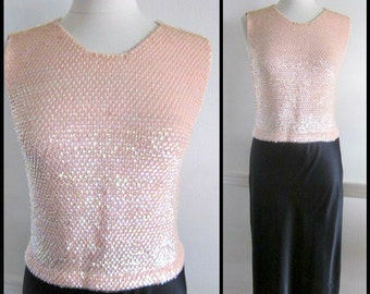 May include: A sleeveless, peach-colored top with a V-neck, covered in small, shimmering sequins. The top is paired with a black, knee-length skirt. The outfit is displayed on a mannequin.