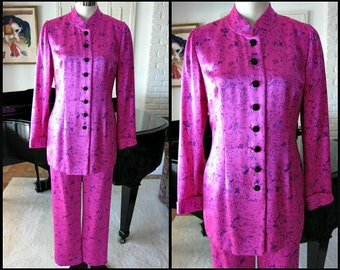 May include: A pink satin pantsuit with a mandarin collar and black buttons. The suit has a floral pattern.
