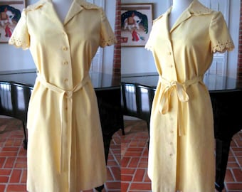 May include: A yellow short-sleeved dress with a button-up front and a tie belt. The dress has a scalloped trim on the sleeves and a collar.