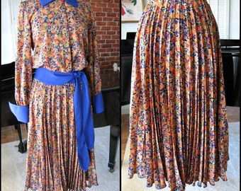 May include: A pleated skirt and matching dress with a floral print in shades of orange, yellow, blue, and brown. The skirt and dress have a blue sash.