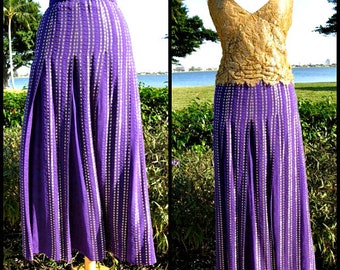 May include: A purple skirt with gold accents. The skirt is pleated and has a high waist. It is made of a shiny fabric.