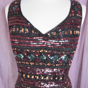 Puede incluir: Un vestido sin mangas de lentejuelas con escote en V. El vestido es negro con lentejuelas rojas, doradas y verdes dispuestas en un patr&oacute;n geom&eacute;trico.