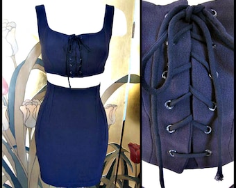 May include: A black two-piece outfit with a lace-up crop top and a skirt. The top has a square neckline and the skirt is fitted.