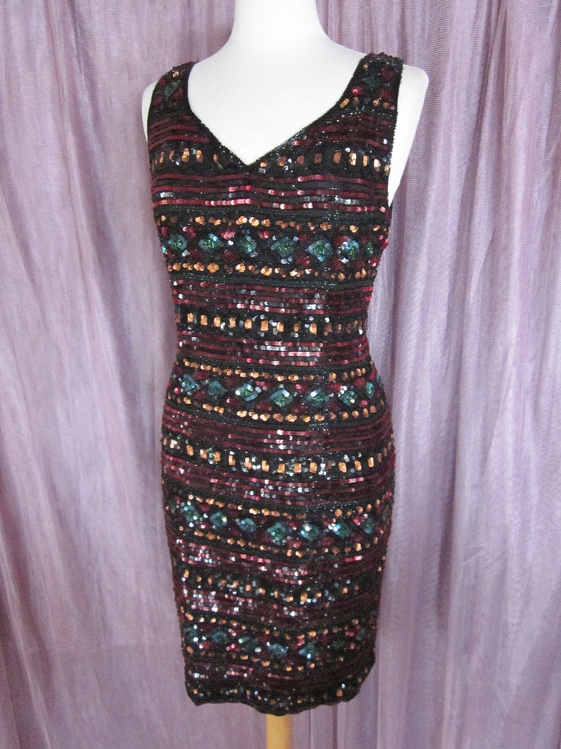 Puede incluir: Un vestido sin mangas de lentejuelas con escote en V. El vestido es negro con lentejuelas rojas, doradas y verdes dispuestas en un patr&oacute;n geom&eacute;trico.