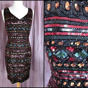 Puede incluir: Un vestido sin mangas de lentejuelas con escote en V. El vestido es negro con lentejuelas rojas, verdes y doradas dispuestas en un patr&oacute;n geom&eacute;trico.