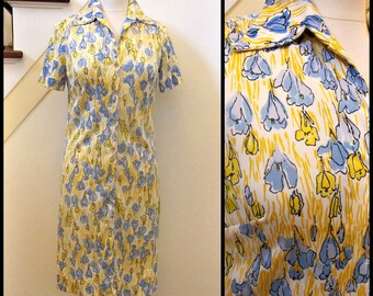 May include: A short-sleeved dress with a collared neckline and button closure. The dress is made of a white fabric with a blue and yellow floral print.