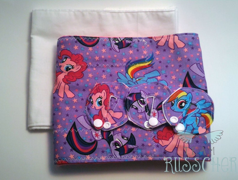 May include: Purple fabric diaper cover with a My Little Pony print featuring pink, blue, and rainbow colors. The cover has three white snaps and a white fabric lining.
