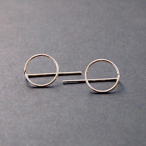 May include: A pair of gold-toned earrings with a simple circle design. Each earring features a thin, horizontal bar across the center of the circle.