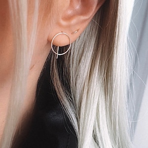 May include: A close-up of a person's ear with a silver hoop earring and a silver bar earring. The earrings are simple and minimalist.