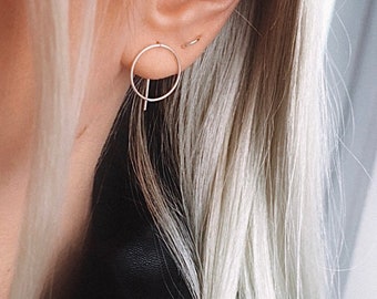 May include: A close-up of a person's ear with a silver hoop earring and a silver bar earring. The earrings are simple and minimalist.