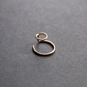May include: A delicate gold-colored ear cuff. The ear cuff features a small, open circle at the top, connected to a larger, open circle that curves around. The jewelry is set against a dark gray background.
