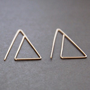 May include: A pair of gold triangle earrings. The earrings are made of thin wire and have a simple, minimalist design.