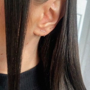 May include: A close-up of a person's ear with three small silver hoop earrings. The earrings are simple and delicate, and they are worn in the upper lobe of the ear.