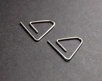 May include: A pair of silver triangle shaped earrings. The earrings are made of thin wire and have a simple, modern design.